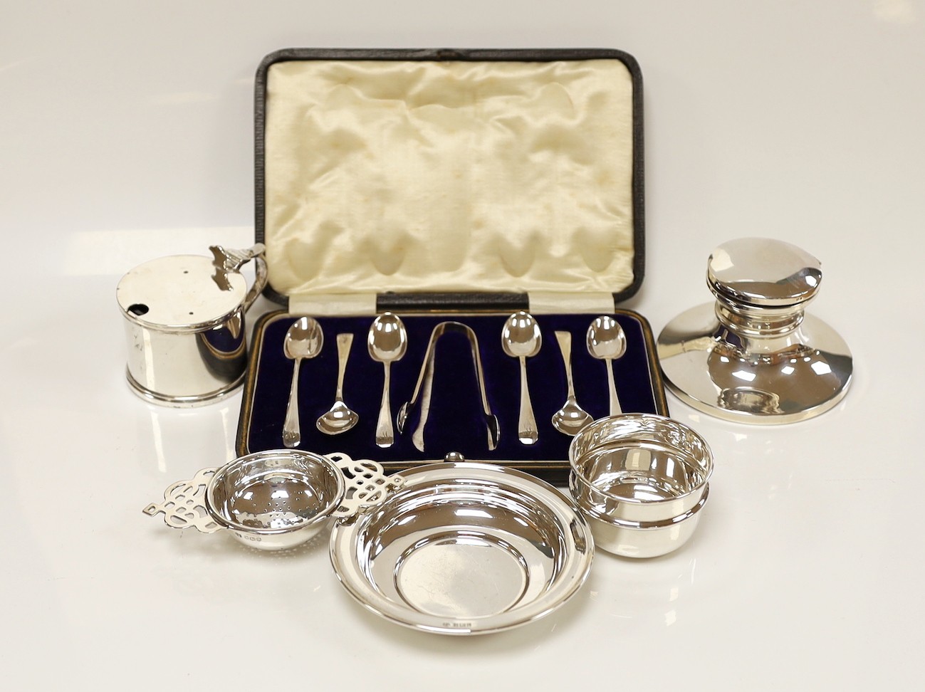 Small silver including a mounted inkwell, tea strainer on stand, mustard pot, small dish and cased set of six coffee spoons with sugar tongs.